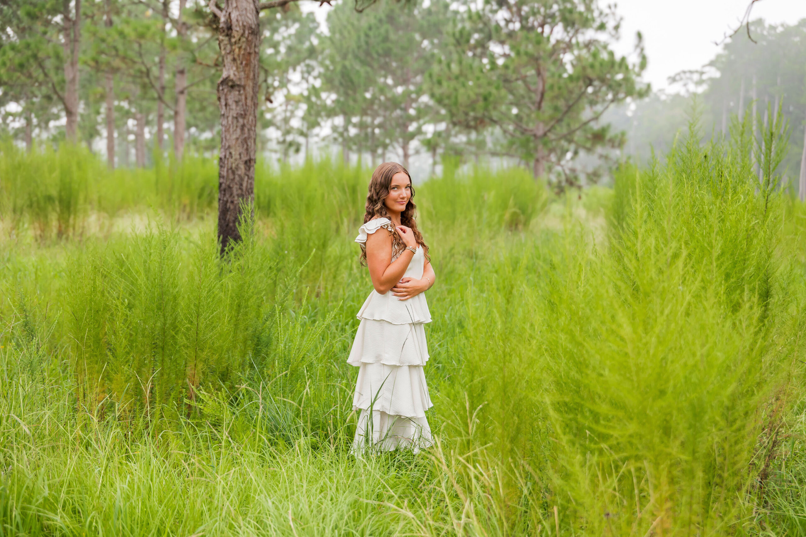 Lilyanne barefoot under Spanish moss trees at Goose Creek State Park, posing in a tiered white dress during her senior portrait session.