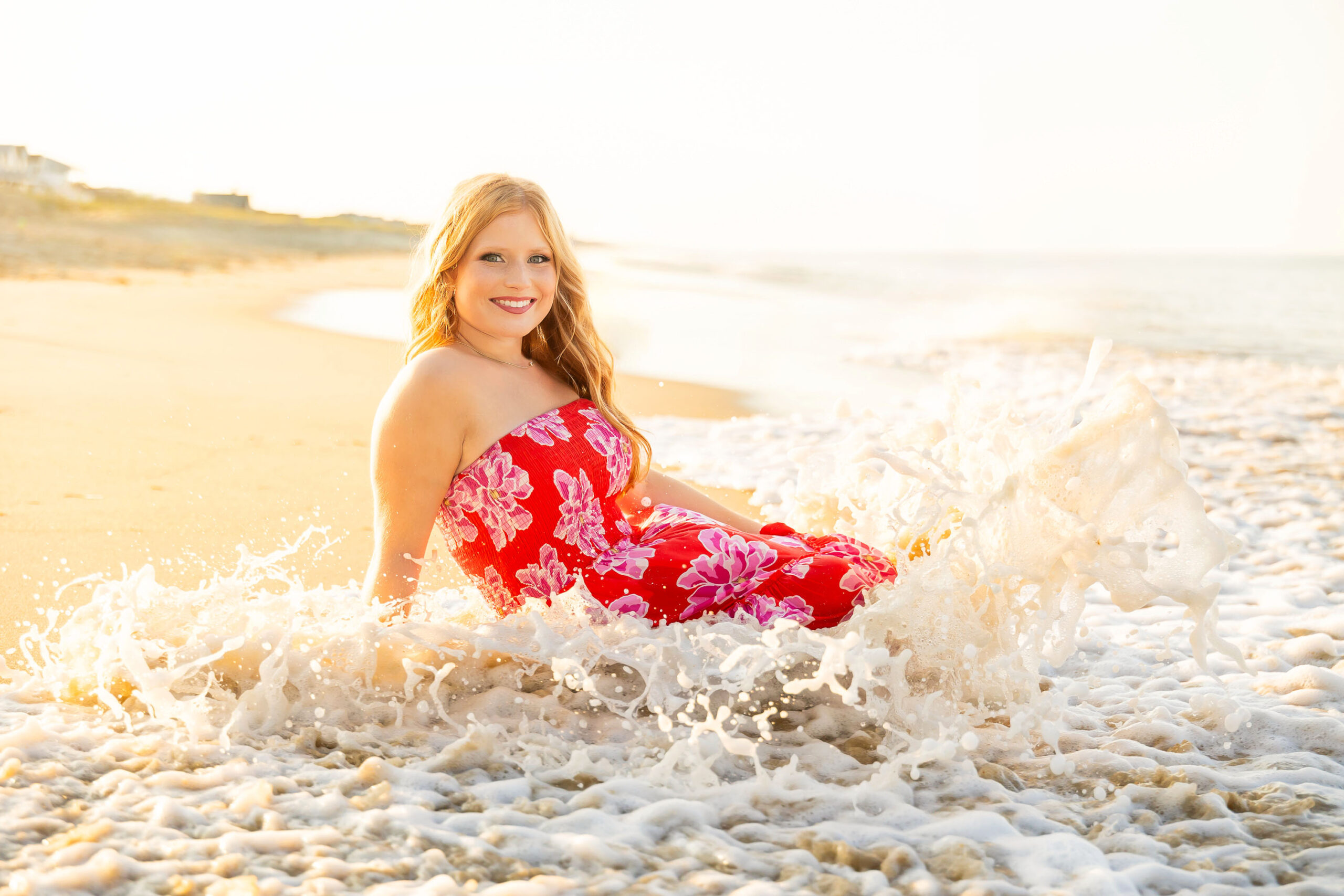 Senior girl laying in the shallow ocean waves wearing an orange floral dress during sunset at Kitty Hawk Fishing Pier.