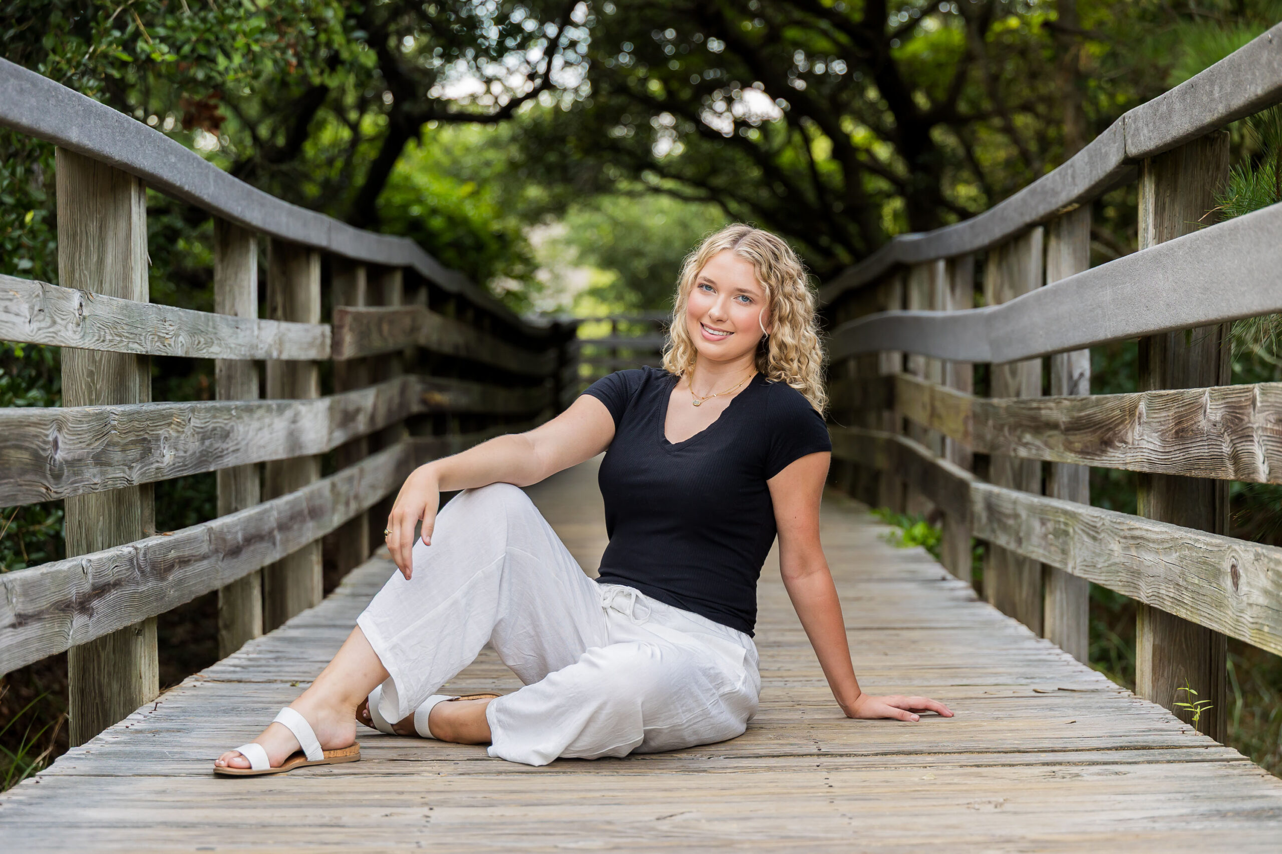 Lia posing among the sand dunes and sea oats at Jockey's Ridge, wearing a black top and white pants, with tall grasses and driftwood around her.
