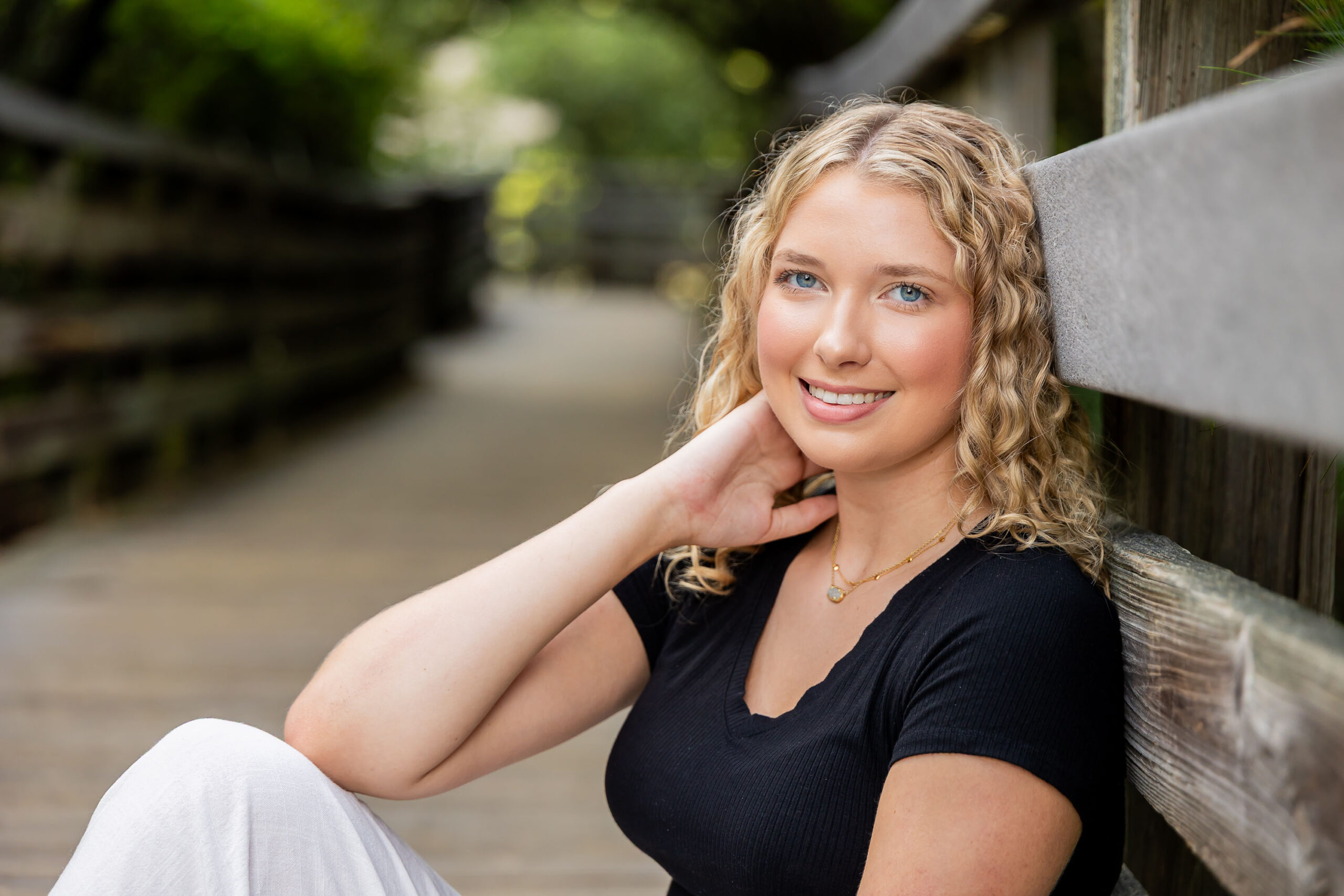 Lia posing among the sand dunes and sea oats at Jockey's Ridge, wearing a black top and white pants, with tall grasses and driftwood around her.