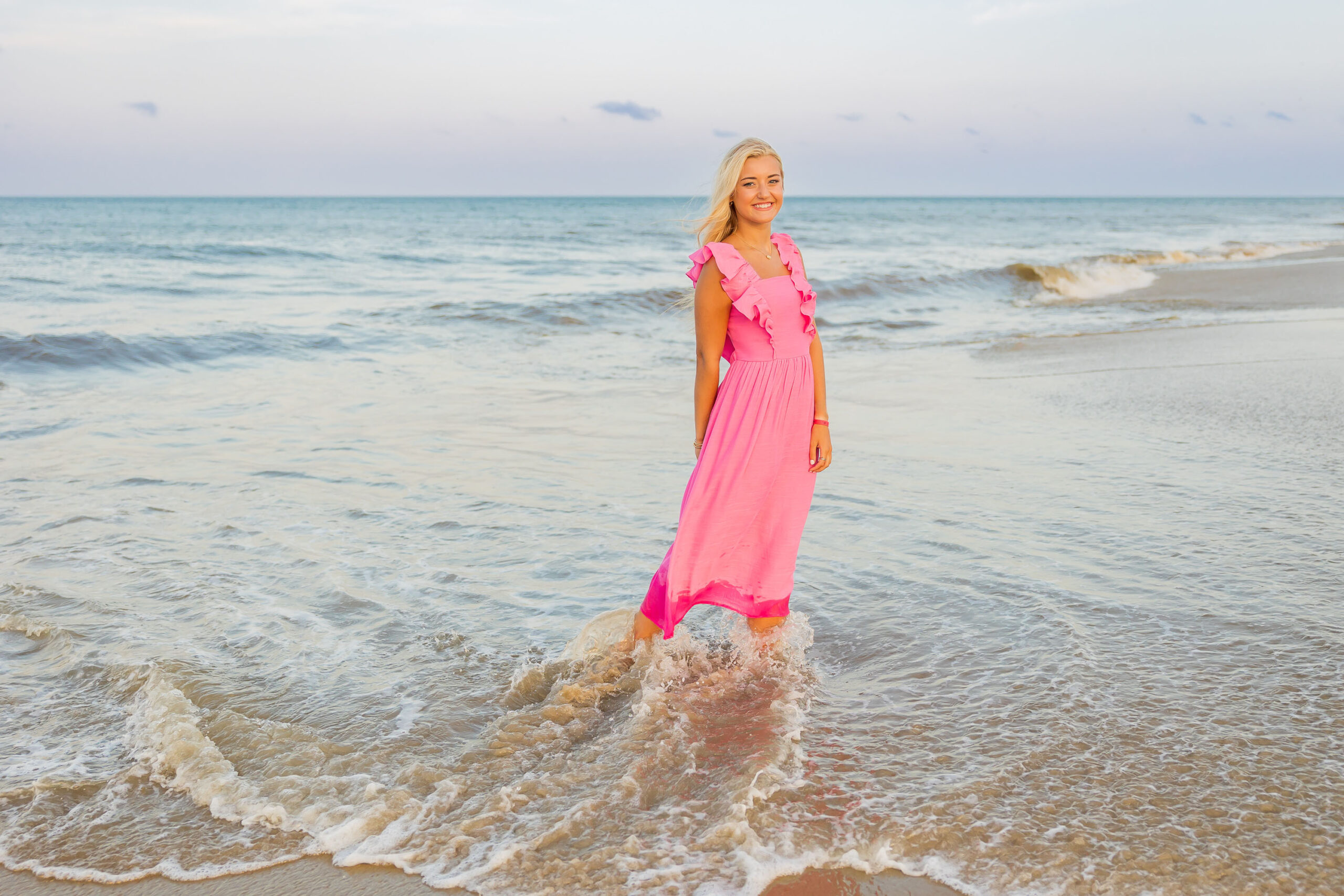 Senior girl smiling with cotton candy sky behind her during Outer Banks beach senior session at Coquina Beach.