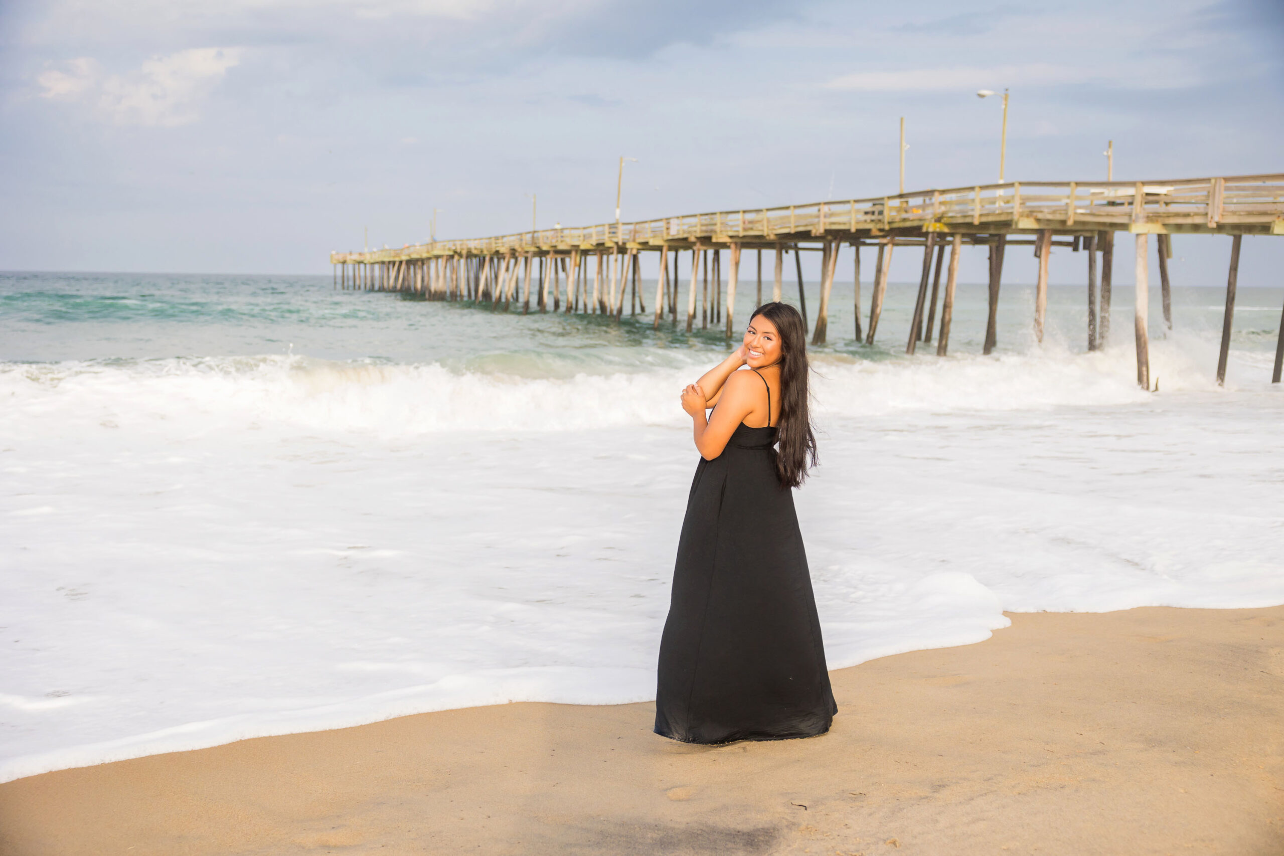 High school senior girl standing beside Nags Head Fishing Pier during Outer Banks senior photo session.