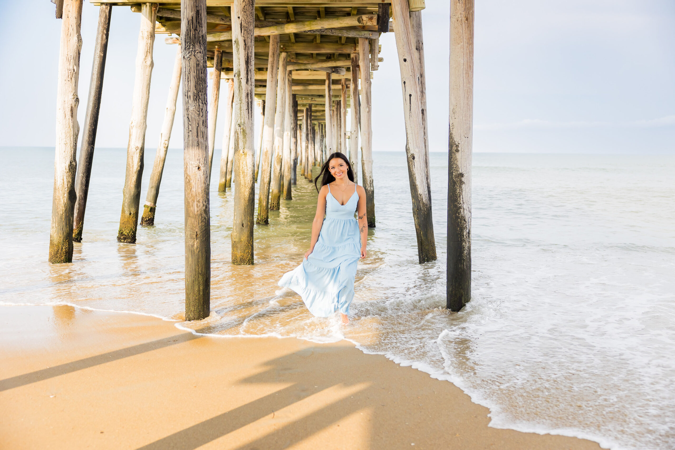 Dramatic senior portrait under Nags Head Pier with wooden beams and ocean backdrop in OBX.