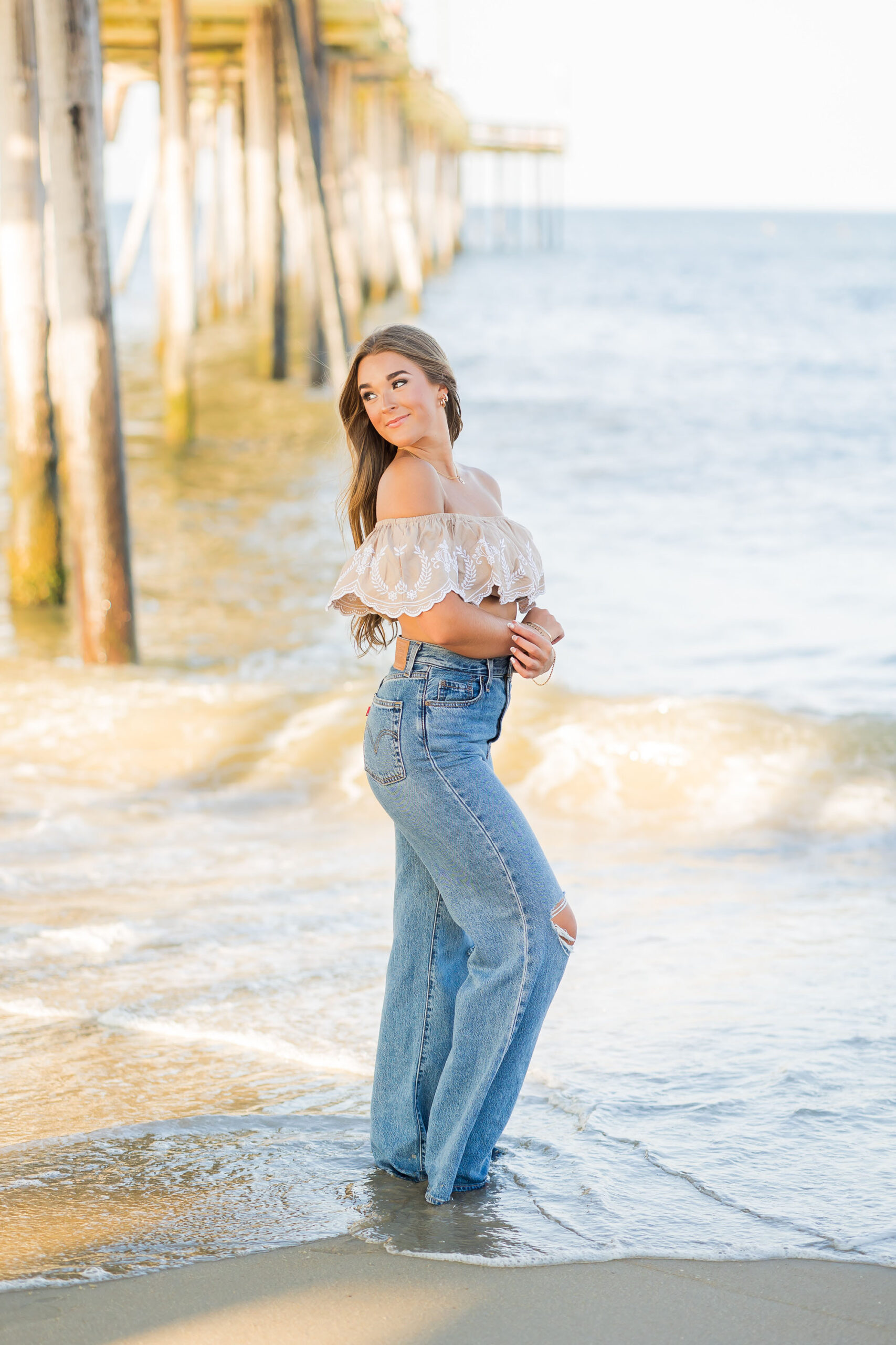 Dramatic senior portrait under Nags Head Pier with wooden beams and ocean backdrop in OBX.