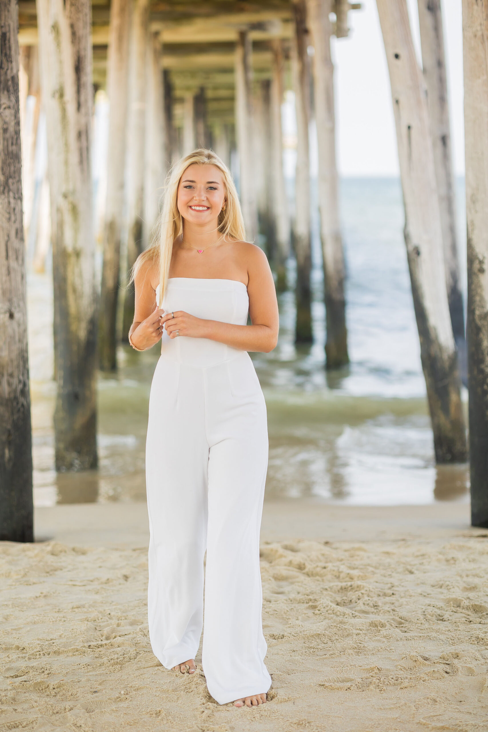 High school senior girl standing beside Nags Head Fishing Pier during Outer Banks senior photo session.