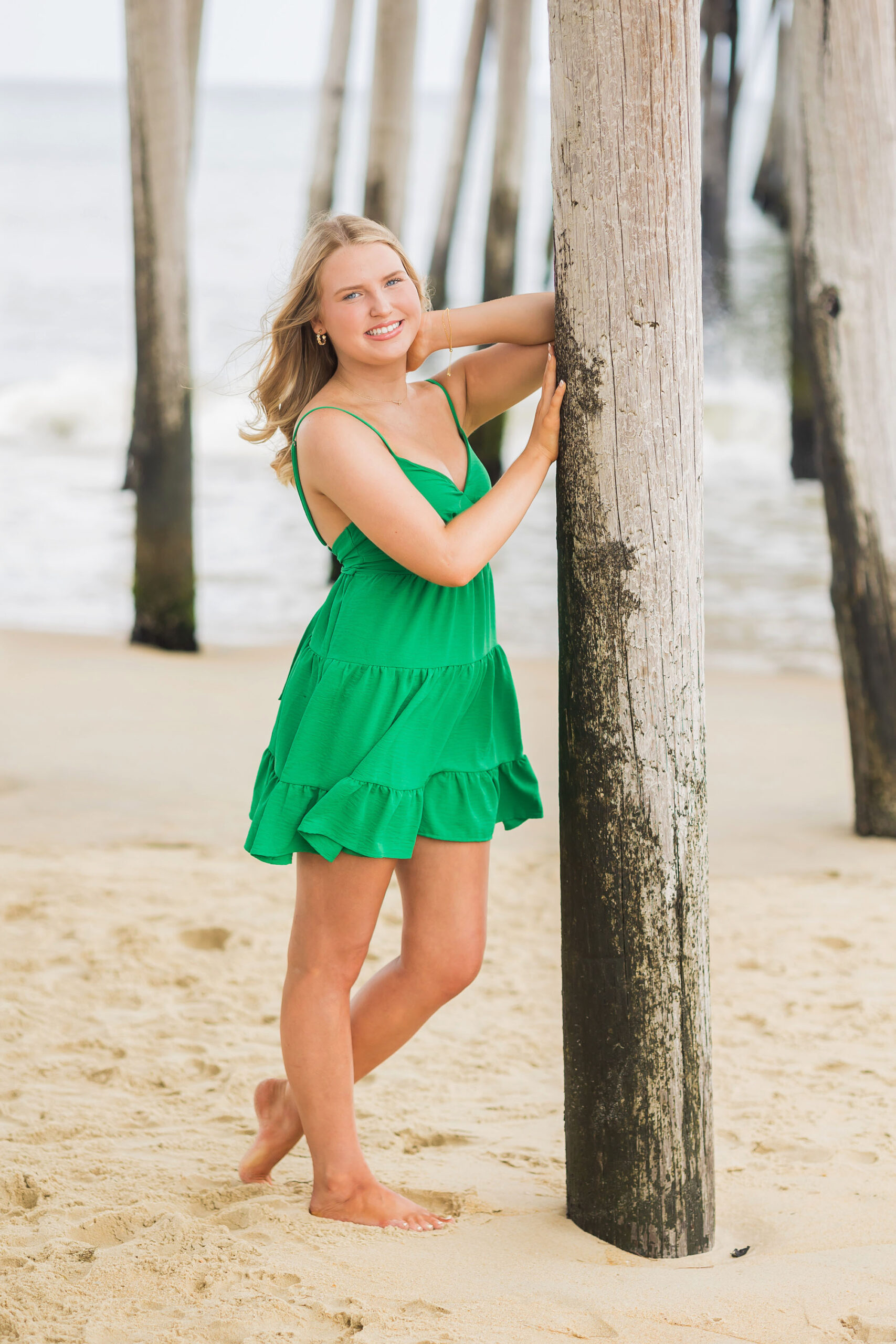 Dramatic senior portrait under Nags Head Pier with wooden beams and ocean backdrop in OBX.