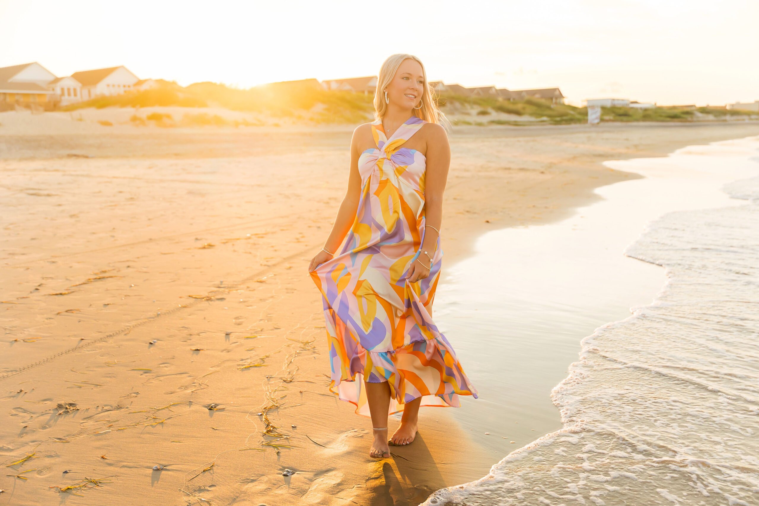 Annabelle walking along Nags Head Beach near Jennette’s Pier in a colorful maxi dress, golden sunshine glowing behind her.