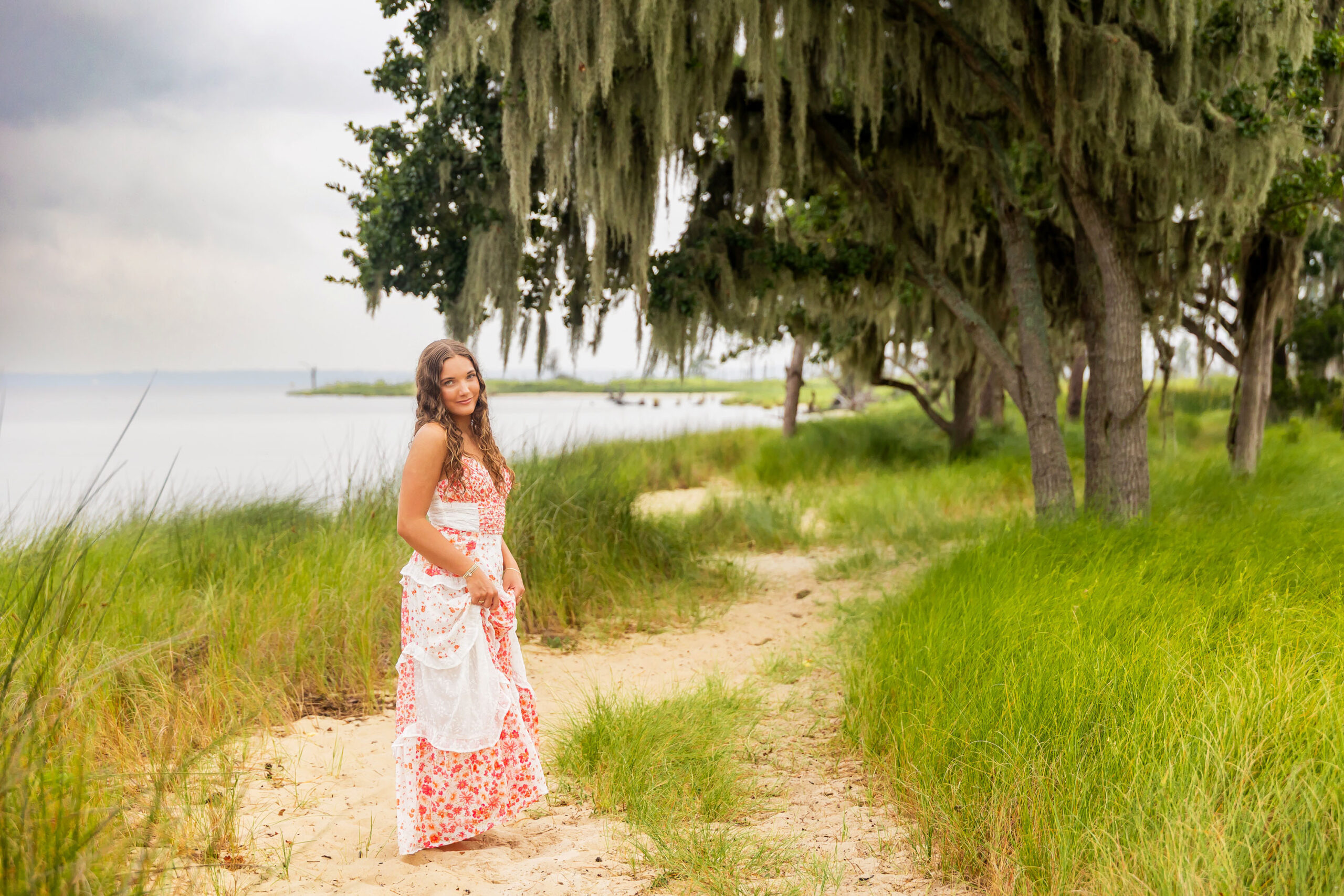 Lilyanne standing in the water at Goose Creek State Park during her senior portrait session, wearing a floral dress and embracing the misty weather.