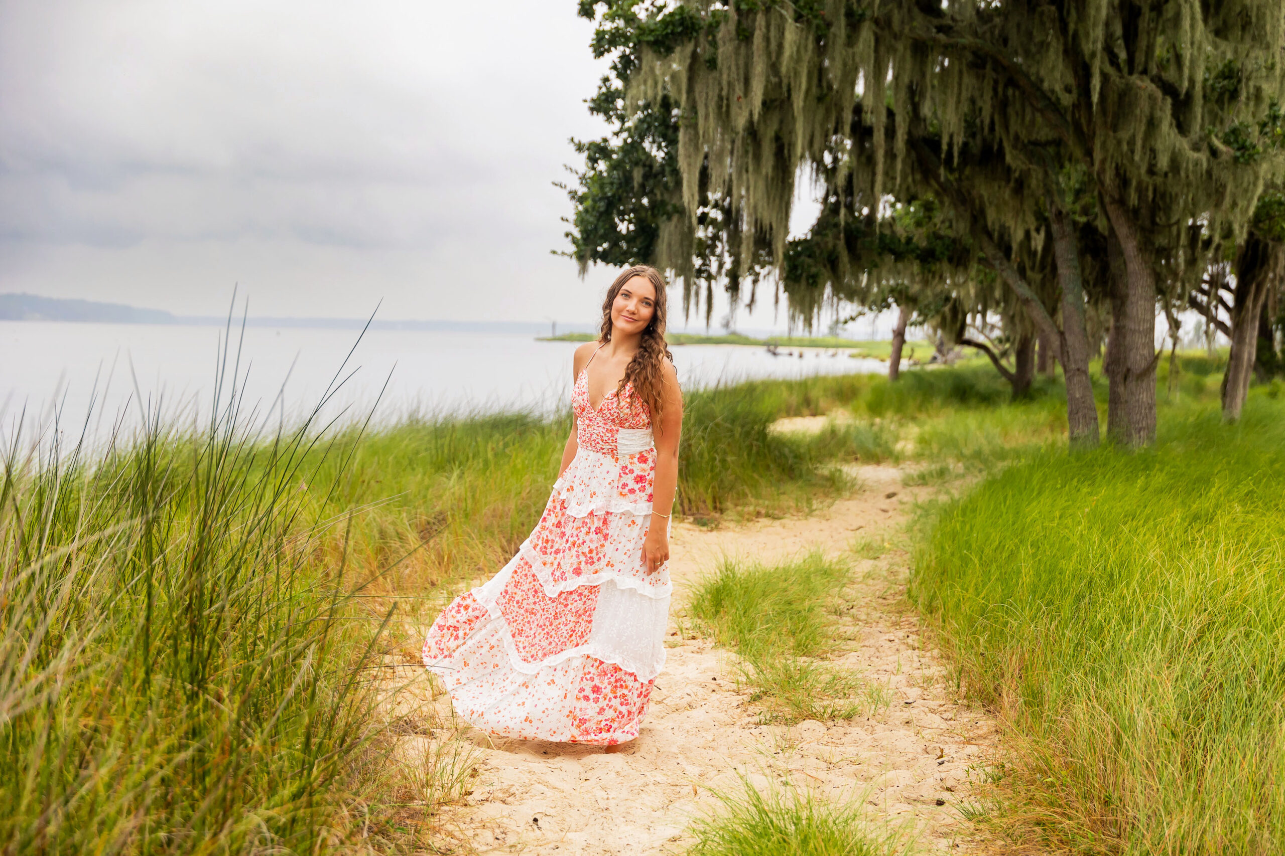 Lilyanne standing in the water at Goose Creek State Park during her senior portrait session, wearing a floral dress and embracing the misty weather.