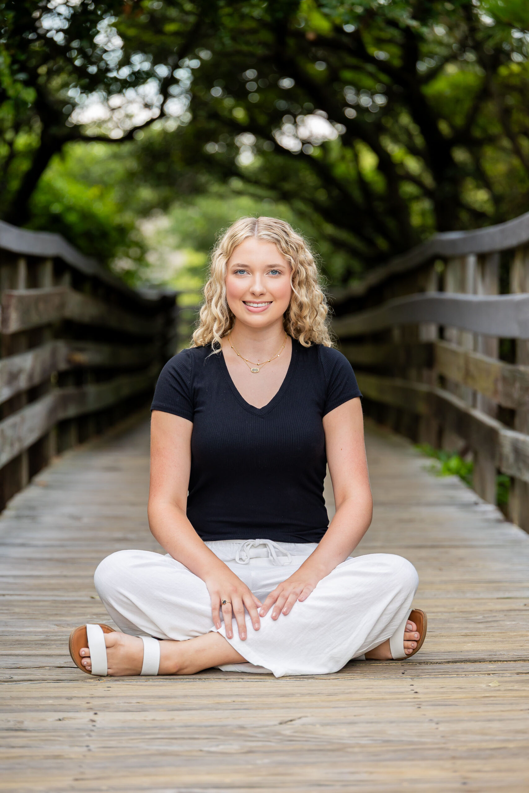 Lia posing among the sand dunes and sea oats at Jockey's Ridge, wearing a black top and white pants, with tall grasses and driftwood around her.